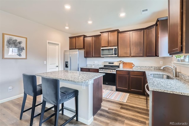 kitchen with a sink, a kitchen island, appliances with stainless steel finishes, a breakfast bar area, and light wood finished floors