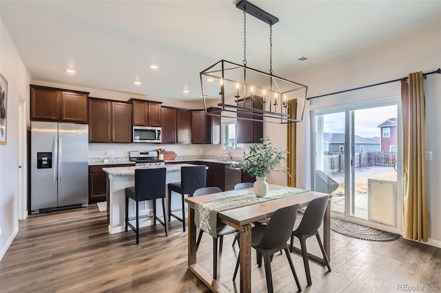 kitchen with dark brown cabinetry, a center island, wood finished floors, and stainless steel appliances