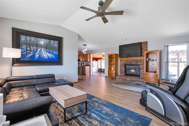 living area with a wealth of natural light, a brick fireplace, vaulted ceiling, and wood finished floors