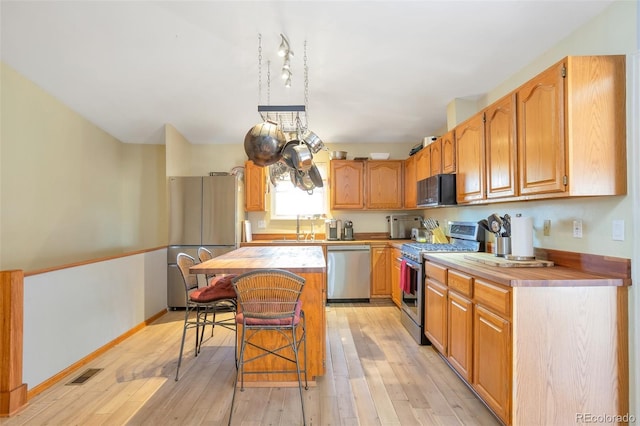 kitchen with a breakfast bar, a sink, light wood-style floors, appliances with stainless steel finishes, and a center island