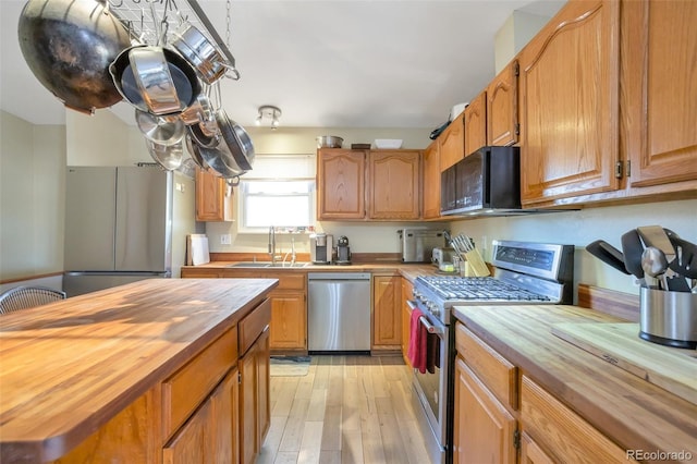 kitchen with light wood-style floors, stainless steel appliances, wooden counters, and a sink