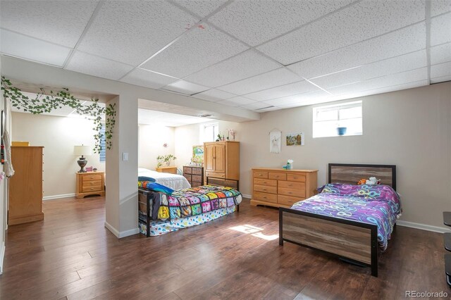 bedroom with baseboards, a drop ceiling, and wood finished floors