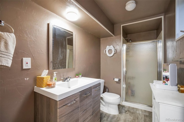 bathroom featuring wood finished floors, a stall shower, vanity, and toilet