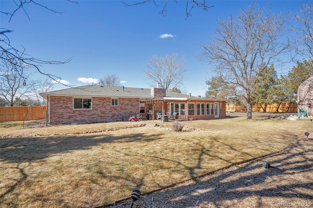 back of property with a sunroom, a chimney, fence, a yard, and brick siding