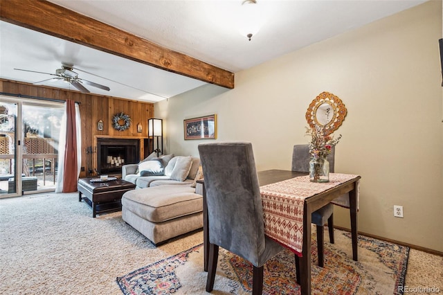 dining space featuring beam ceiling, carpet floors, ceiling fan, and wood walls