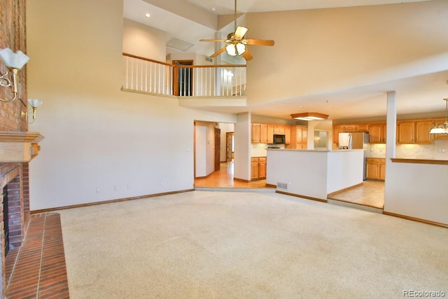 unfurnished living room with ceiling fan, a towering ceiling, light colored carpet, and a fireplace