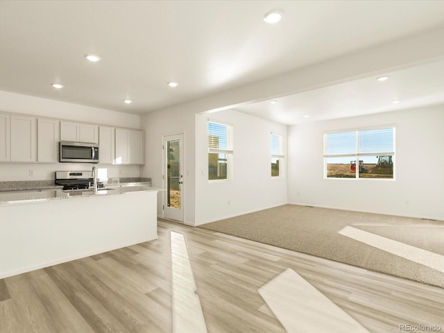 kitchen featuring sink, white cabinetry, light wood-type flooring, appliances with stainless steel finishes, and light stone countertops