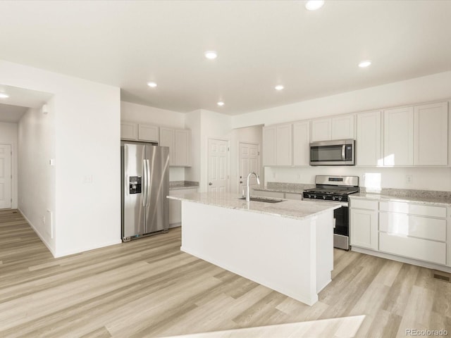 kitchen featuring sink, appliances with stainless steel finishes, white cabinetry, light stone counters, and an island with sink