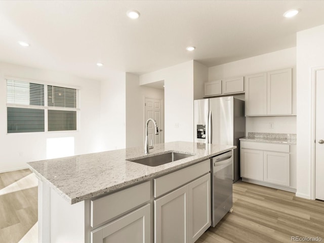 kitchen with sink, a kitchen island with sink, stainless steel appliances, light stone counters, and light wood-type flooring