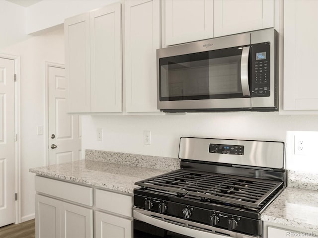 kitchen featuring white cabinetry, appliances with stainless steel finishes, dark hardwood / wood-style floors, and light stone counters