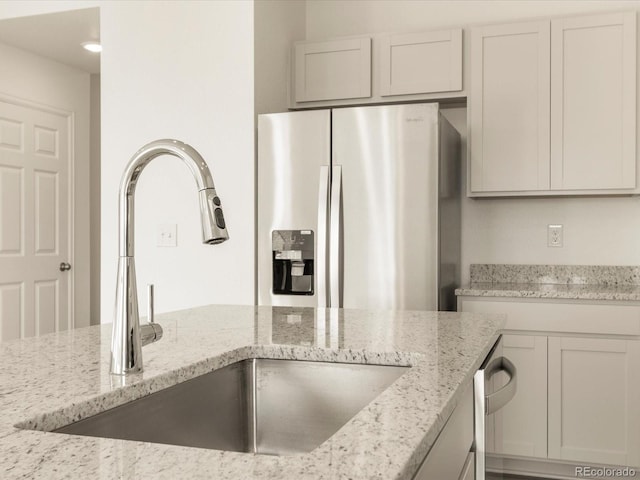 kitchen with light stone counters, sink, white cabinetry, and stainless steel fridge