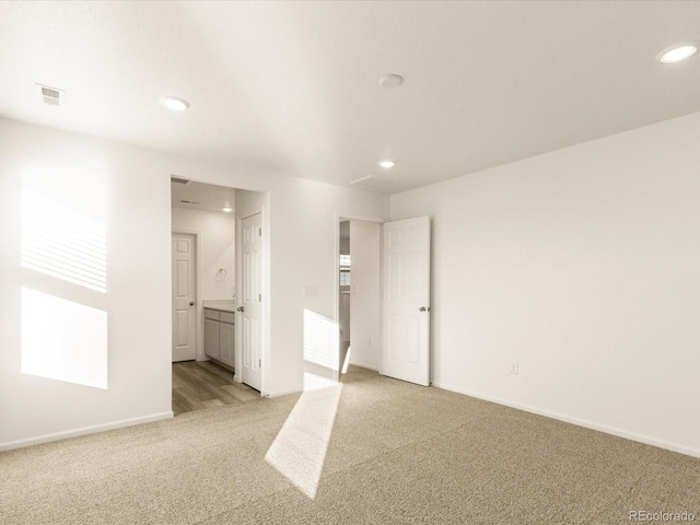 unfurnished bedroom featuring multiple windows, ensuite bath, and light colored carpet