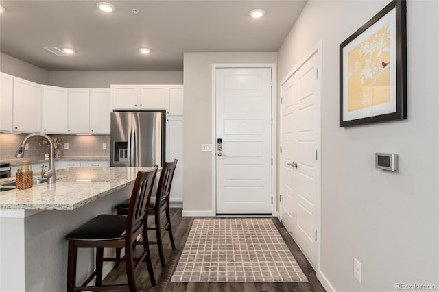 kitchen with stainless steel fridge with ice dispenser, decorative backsplash, sink, white cabinets, and a breakfast bar