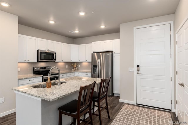 kitchen featuring a kitchen breakfast bar, white cabinets, stainless steel appliances, light stone counters, and a center island with sink