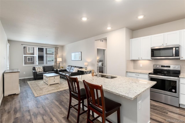 kitchen with a kitchen bar, appliances with stainless steel finishes, white cabinets, an island with sink, and light stone counters