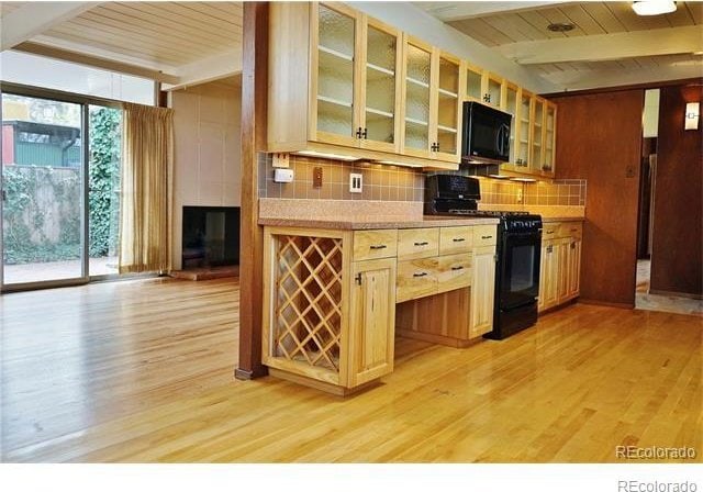 kitchen featuring light wood-type flooring, backsplash, beam ceiling, and black appliances