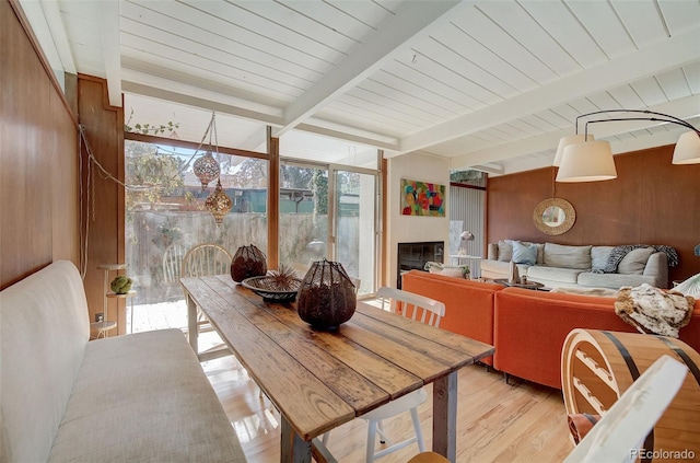 dining area featuring beamed ceiling, light wood-type flooring, and wooden walls