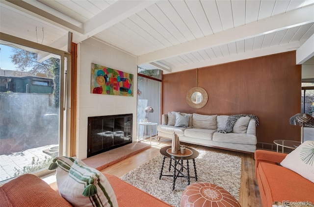 living room with a fireplace, wood walls, wooden ceiling, beam ceiling, and hardwood / wood-style floors