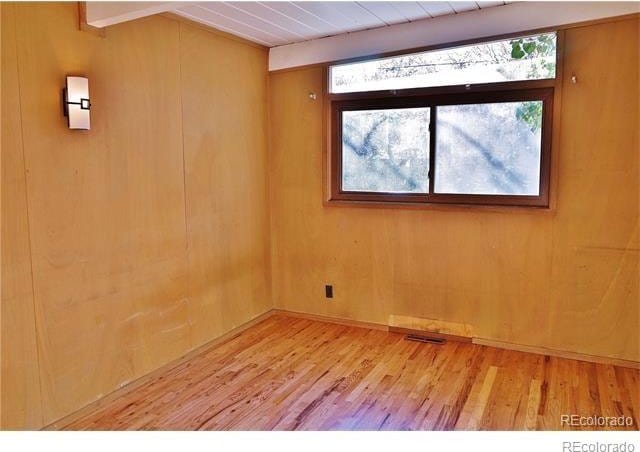 spare room featuring light hardwood / wood-style flooring, wooden walls, beam ceiling, and wood ceiling