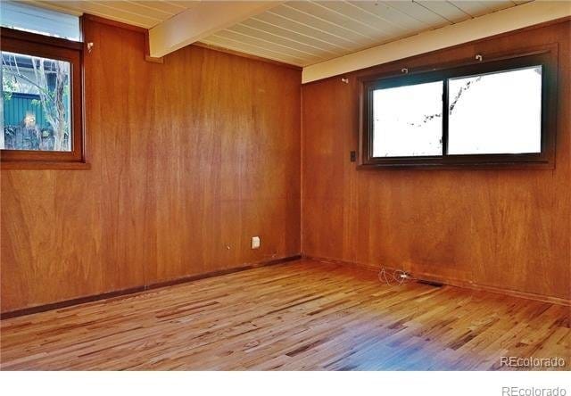 unfurnished room with wooden ceiling, beamed ceiling, wood walls, and light hardwood / wood-style flooring