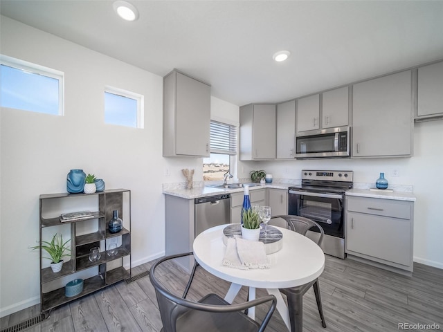 kitchen with appliances with stainless steel finishes, light wood-type flooring, gray cabinetry, and sink