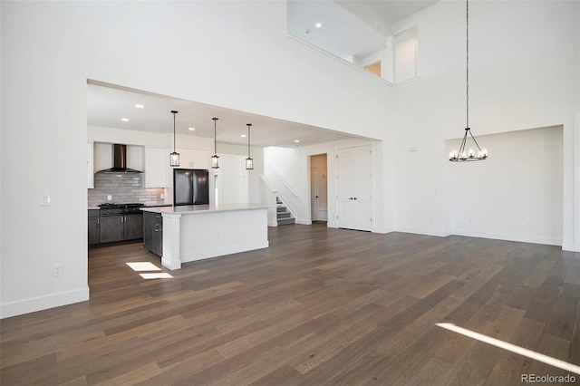 kitchen with an inviting chandelier, dark wood-style flooring, wall chimney exhaust hood, tasteful backsplash, and black fridge