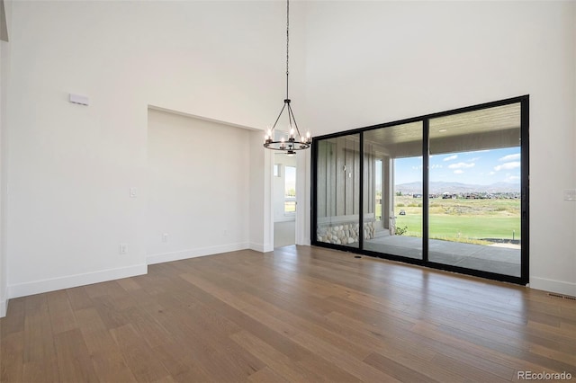 unfurnished room with visible vents, baseboards, a high ceiling, an inviting chandelier, and wood finished floors