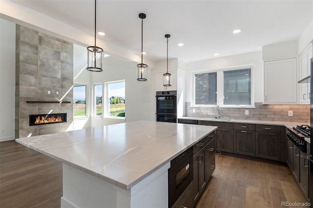 kitchen with backsplash, light stone counters, a fireplace, black appliances, and a sink