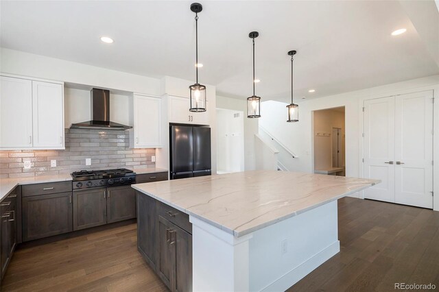 kitchen featuring dark wood-type flooring, wall chimney range hood, gas stovetop, and freestanding refrigerator