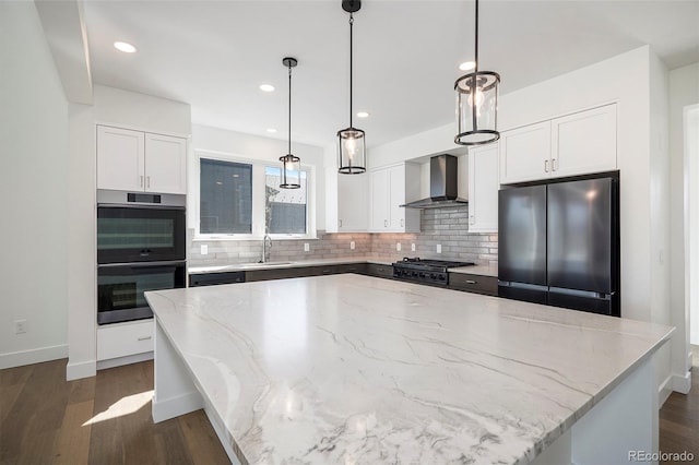 kitchen featuring a sink, a spacious island, appliances with stainless steel finishes, wall chimney range hood, and light stone countertops