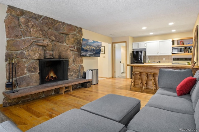 living room featuring light hardwood / wood-style floors, a stone fireplace, and a textured ceiling