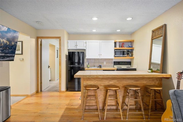 kitchen featuring a breakfast bar, white range with electric stovetop, black refrigerator, decorative backsplash, and tile counters