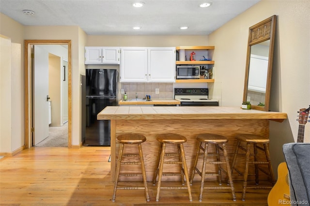 kitchen featuring decorative backsplash, black fridge, electric range, white cabinetry, and tile counters