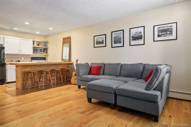 living room featuring light wood-type flooring, a textured ceiling, and a baseboard heating unit