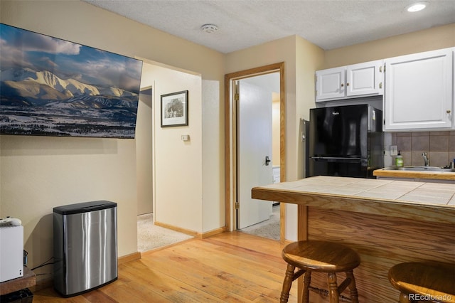 kitchen featuring white cabinetry, sink, black fridge, light hardwood / wood-style flooring, and tile countertops