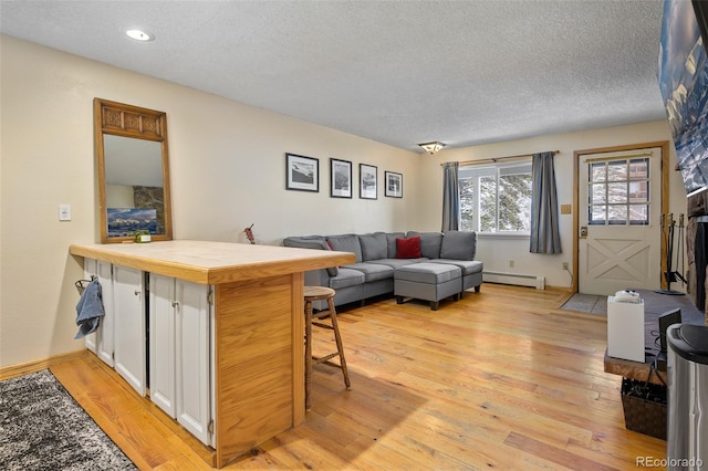 living room with a textured ceiling, baseboard heating, and light hardwood / wood-style flooring