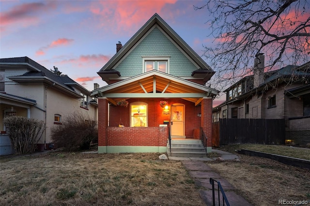 victorian house with a porch, fence, brick siding, and a front yard