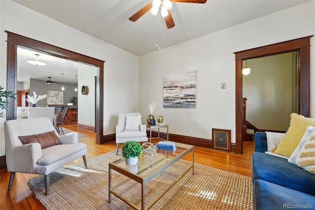 living area with light wood-style flooring, a ceiling fan, and baseboards