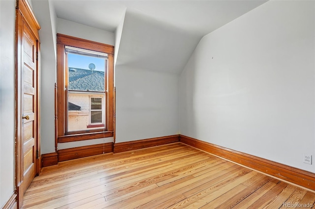 empty room with lofted ceiling, light wood-type flooring, and baseboards