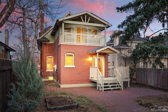 view of front facade with a patio, a balcony, fence, a vegetable garden, and brick siding