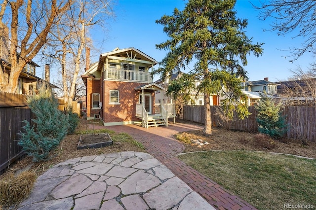 rear view of property featuring a balcony, fence, and brick siding