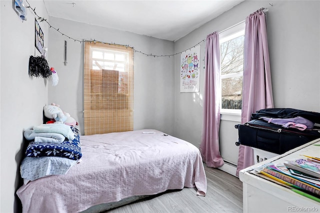 bedroom with baseboard heating, light hardwood / wood-style flooring, and multiple windows