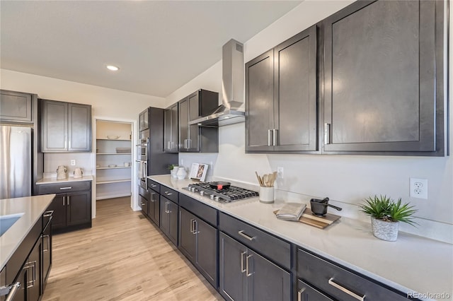 kitchen featuring light wood-style floors, appliances with stainless steel finishes, light countertops, wall chimney range hood, and open shelves