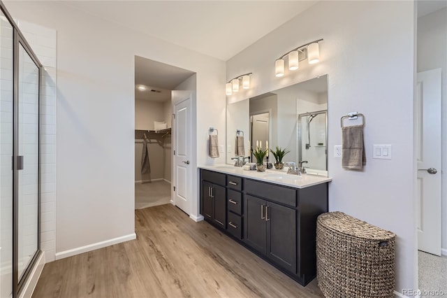 full bath with a spacious closet, wood finished floors, a stall shower, and a sink