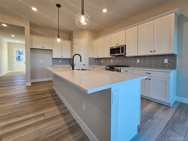 kitchen with stainless steel appliances, a kitchen island with sink, sink, and white cabinets