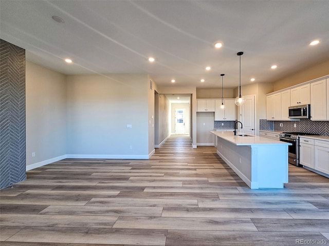 kitchen with light hardwood / wood-style flooring, pendant lighting, stainless steel appliances, a kitchen island with sink, and white cabinets