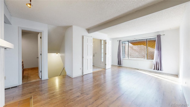 empty room featuring hardwood / wood-style flooring, a textured ceiling, and beam ceiling