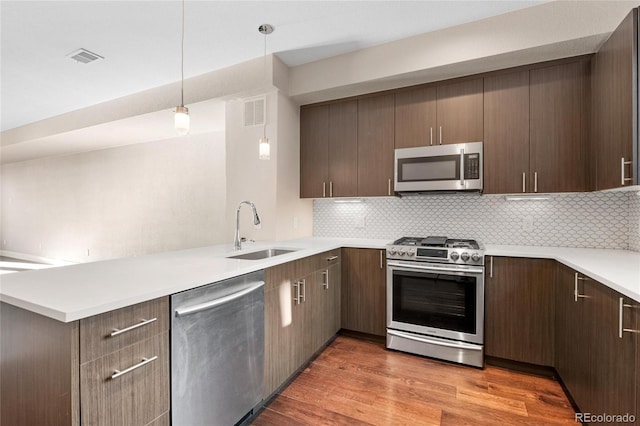 kitchen featuring hardwood / wood-style flooring, hanging light fixtures, stainless steel appliances, sink, and decorative backsplash