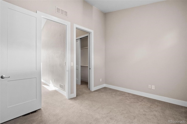 unfurnished bedroom featuring a closet, light colored carpet, and a walk in closet