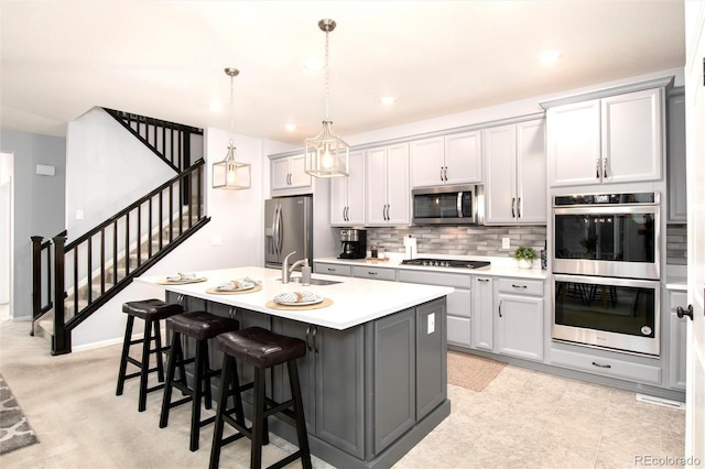 kitchen featuring a center island with sink, gray cabinets, stainless steel appliances, pendant lighting, and sink